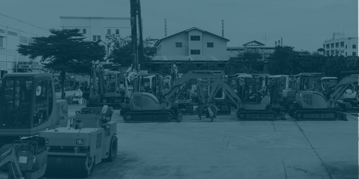 Row of heavy construction equipment including bulldozers, loaders, and excavators lined up on a dirt job site.